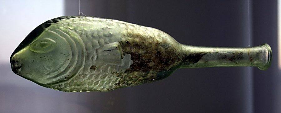 An old green glass bottle shaped like a fish, suspended in mid-air with visible textures and a narrow neck.